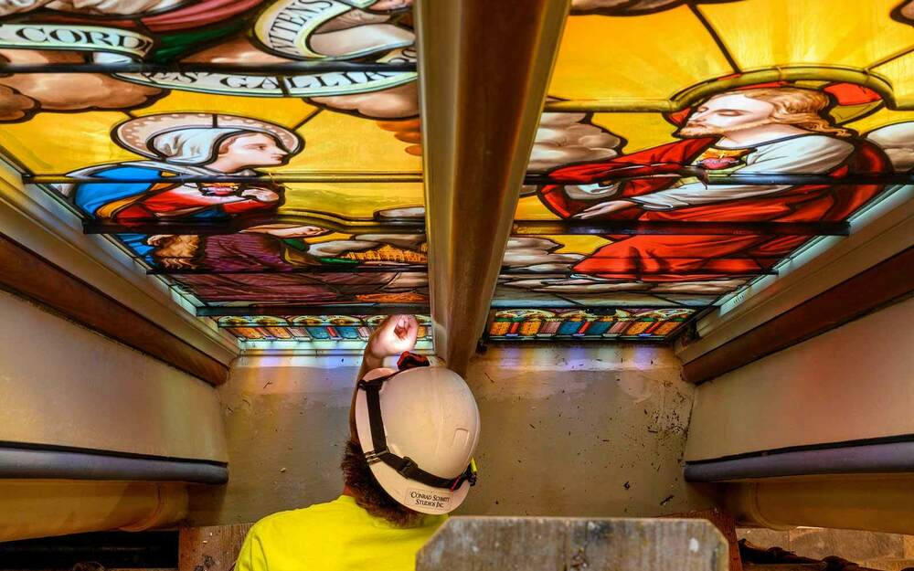 A man leans over as he touches a stained glass window depicting the Virgin Mary and Jesus as part of restoration work.