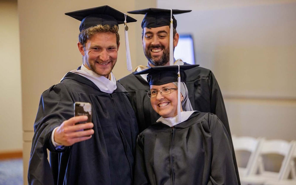 Three people wearing black caps and gowns take a selfie.