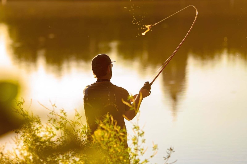 A man fishes on a lake during sunset.