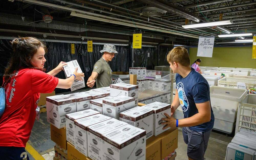 Three people pass boxes inside of a warehouse.