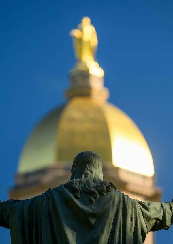 The Sacred Heart Jesus statue in focus and the Golden Dome in the background blurred.