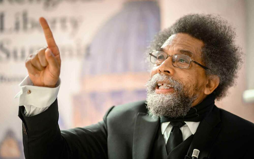 Dr. Cornel West speaks holding hit arm up and pointing his finger up.