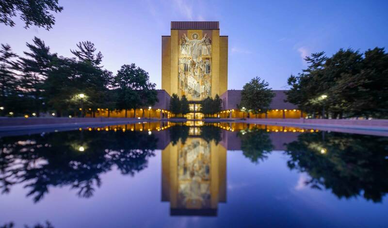 The Hesburgh Library Word of Life Mural, commonly known as Touchdown Jesus reflecting off of the pool in front of the building.