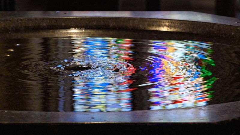 Stained glass window reflected in the Basilica of the Sacred Heart baptismal font.
