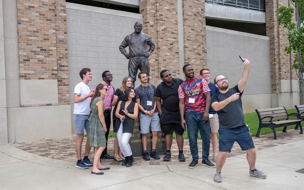 A group of students take a selfie with a statue of Knute Rockne on campus.
