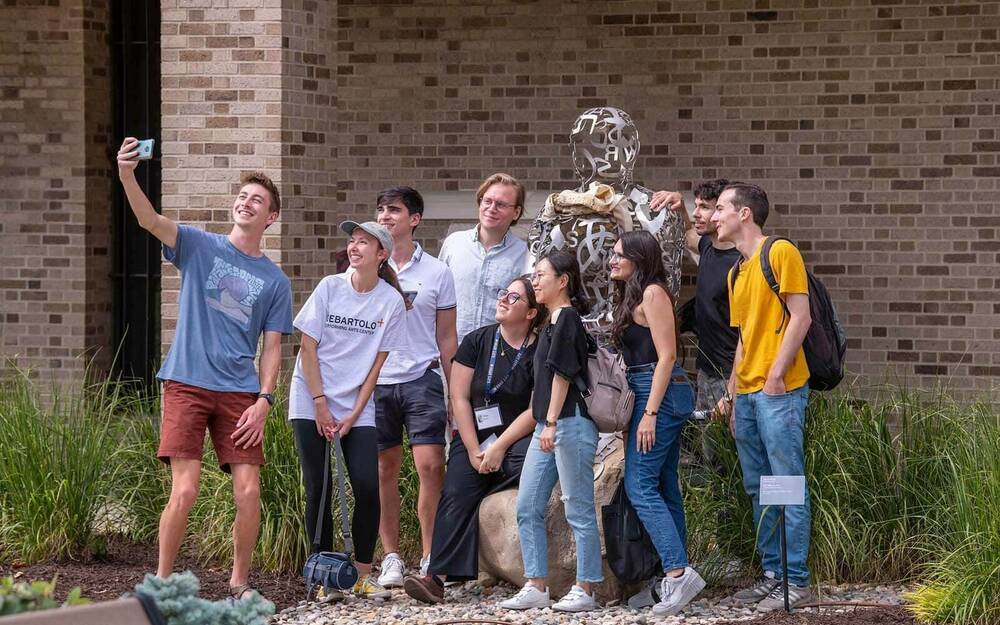 A group of students take a selfie with a sculpture on campus.