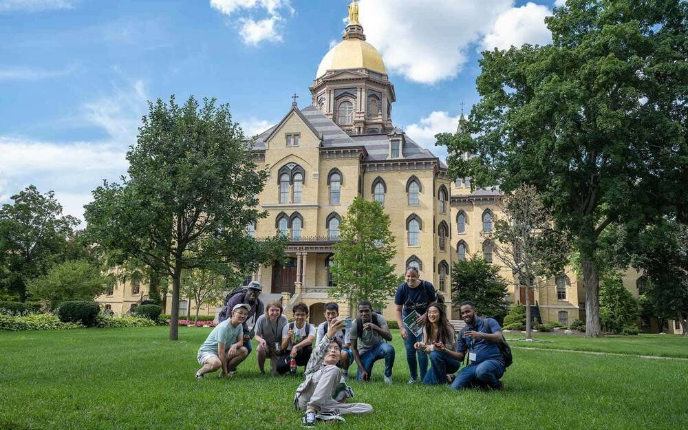 A group of students take a selfie in front of Notre Dame's main building.