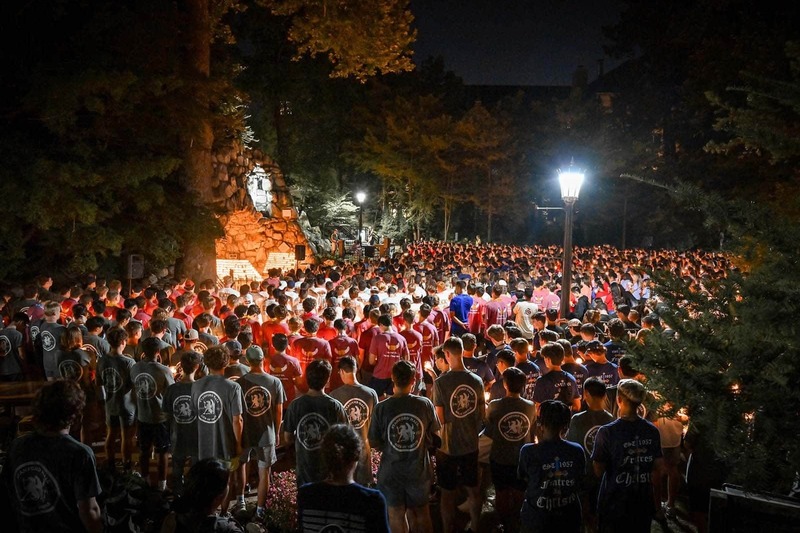 A large group of people gather around the Grotto at night.