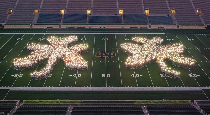 Class of 2026 form two glowing shamrocks on Notre Dame's stadium field by using the flashlight on their phones.
