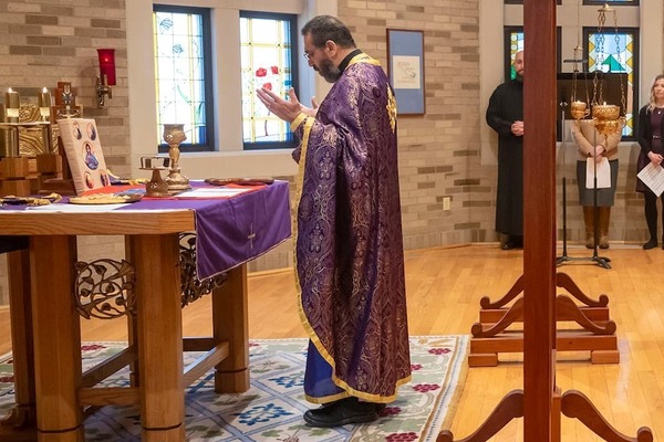 Fr. Khaled Anatolios wears a purple vestment. He stands facing an alter while performing a Byzantine Mass.