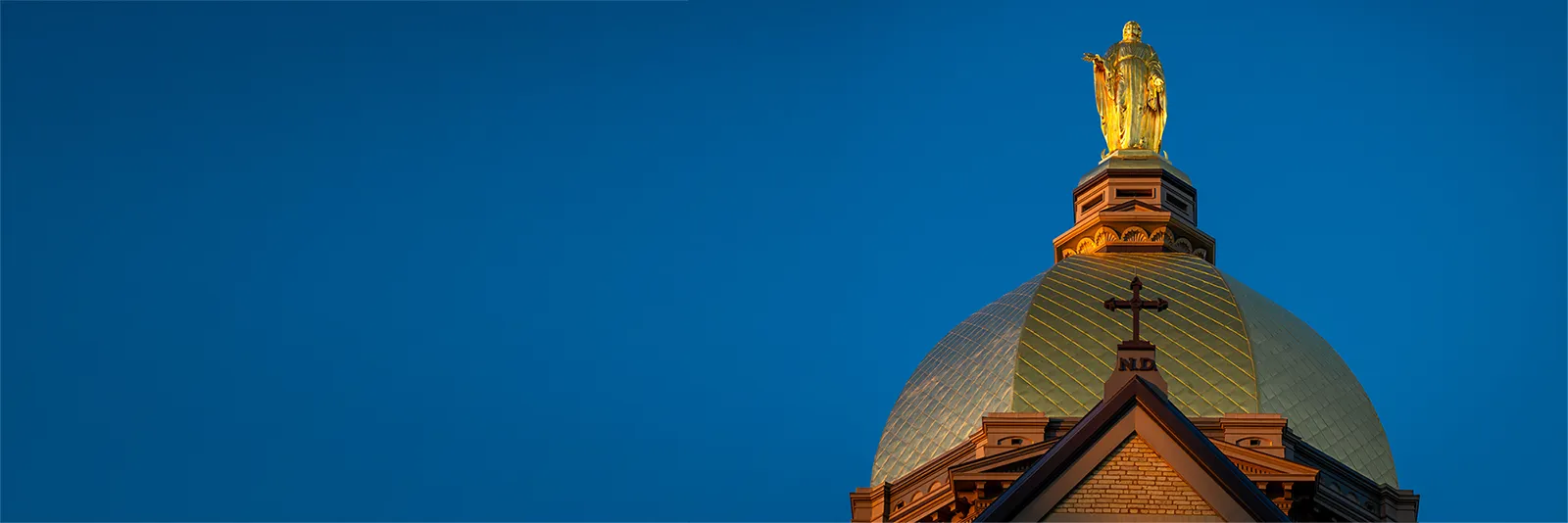 The Golden Dome of the main building on the University of Notre Dame's campus against a blue sky.