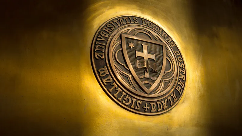 The University of Notre Dame official seal in bronze relief, backlit with warm golden light against a polished brass surface.